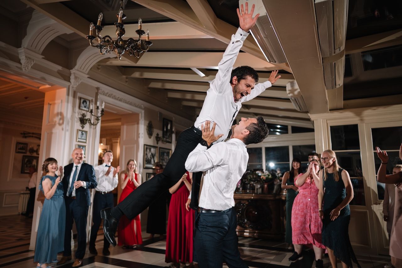 Groomsmen performing dramatic dance lift at elegant wedding reception party.