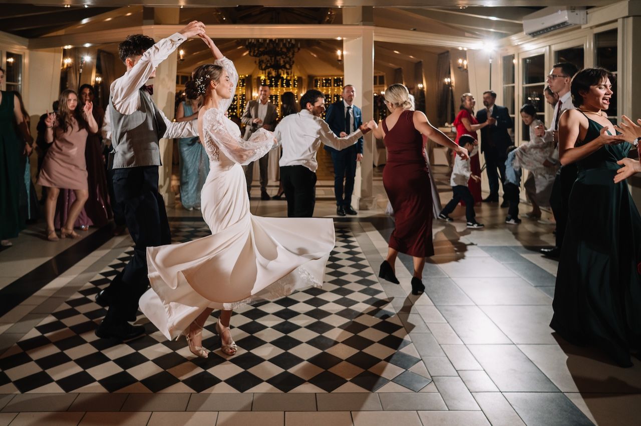Bride and guests dancing energetically on checkered dance floor at wedding reception.