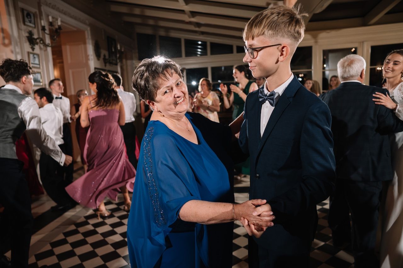 Young man in bow tie dancing with older woman in blue dress at wedding reception.