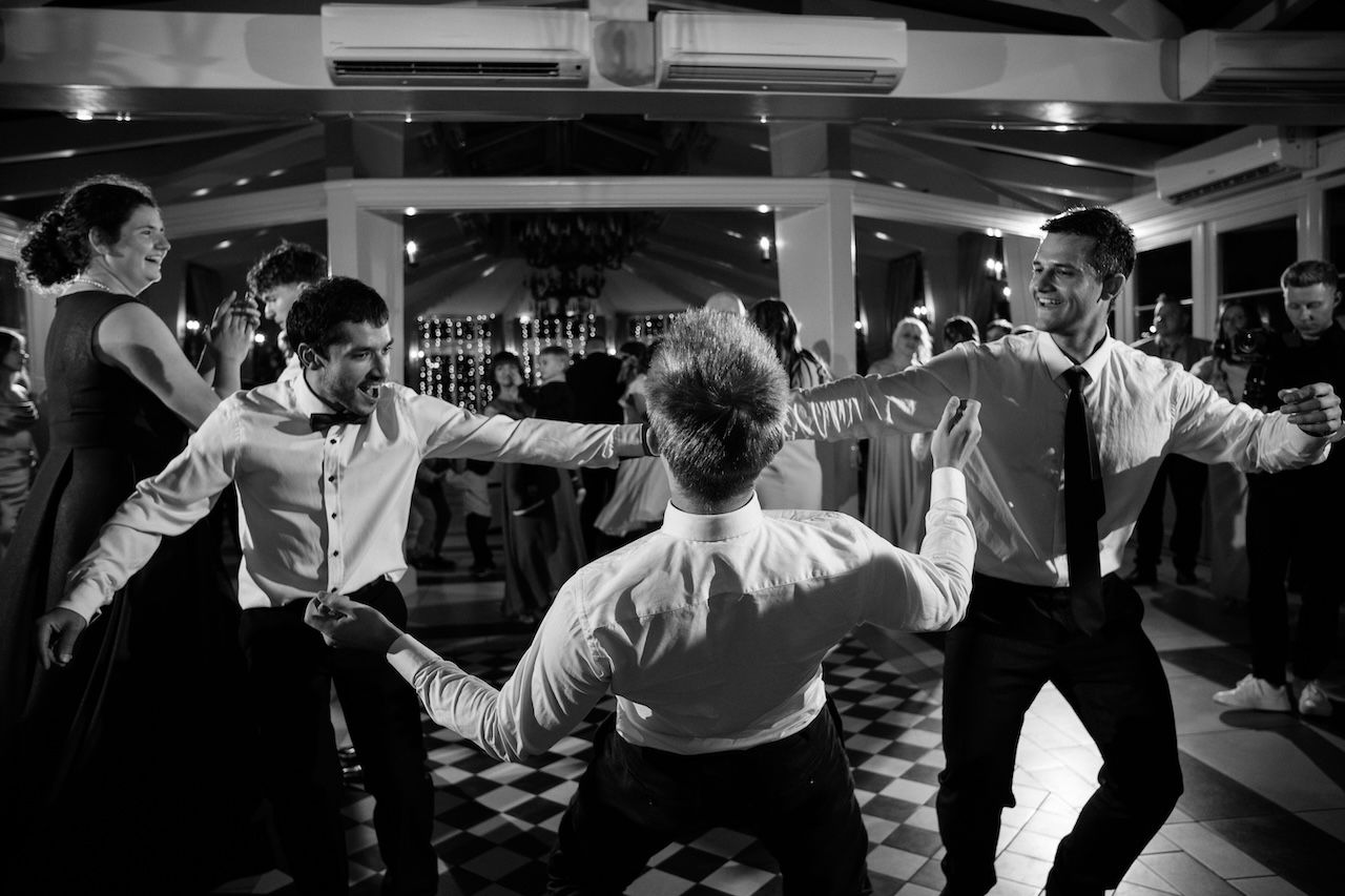 Black and white photo of groomsmen dancing in circle at lively wedding reception.