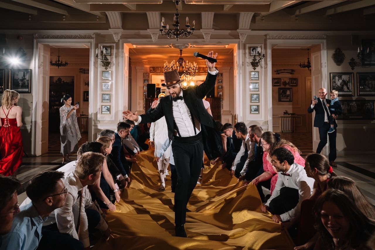 Groom in tuxedo walks through golden fabric tunnel held by wedding guests.