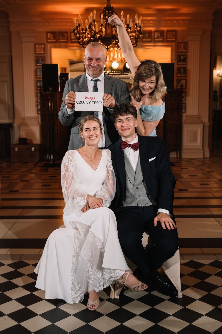Wedding portrait of bride and groom with family holding sign on checkered floor.