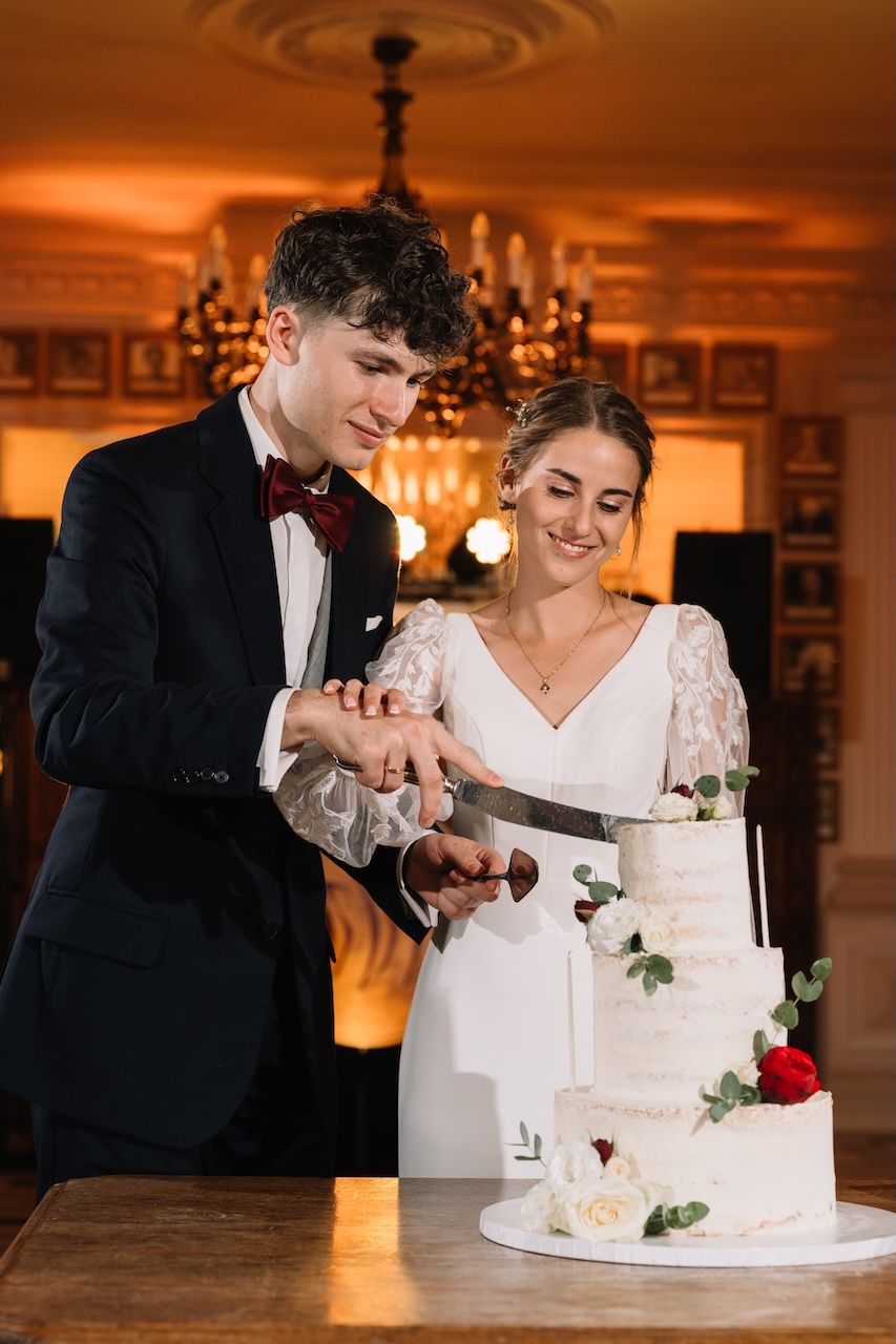 Bride and groom cutting their white floral tiered wedding cake together at their reception.