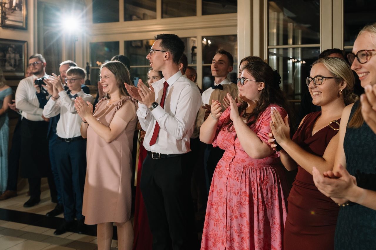 Wedding guests clapping and celebrating during a reception in a beautifully lit elegant venue.