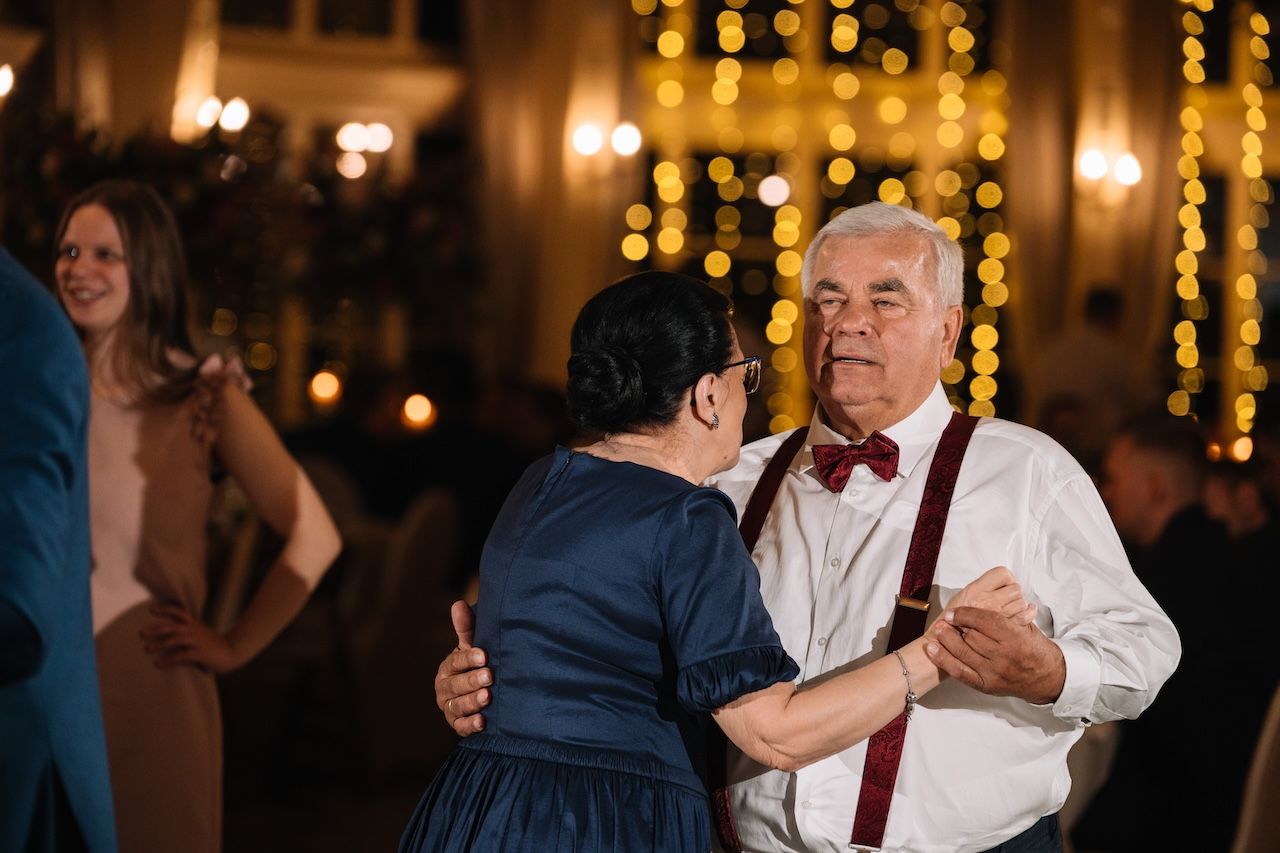 Elderly couple dancing together at a wedding reception with warm bokeh lights in background.