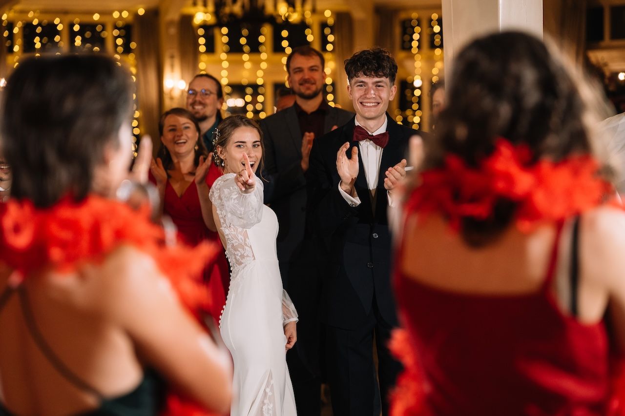 Bride and groom smiling joyfully as guests in red celebrate around them at wedding reception.