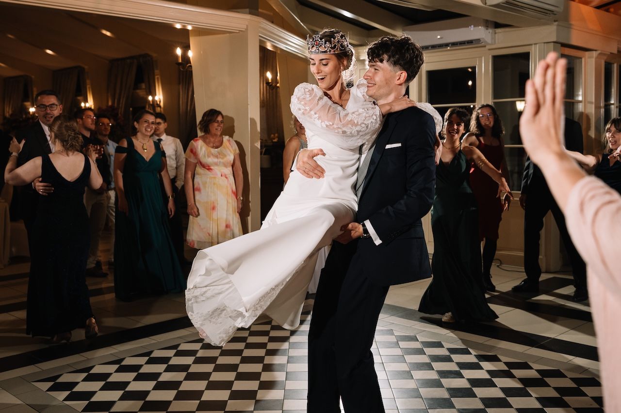Groom lifting bride joyfully on a black and white checkered dance floor at wedding reception.
