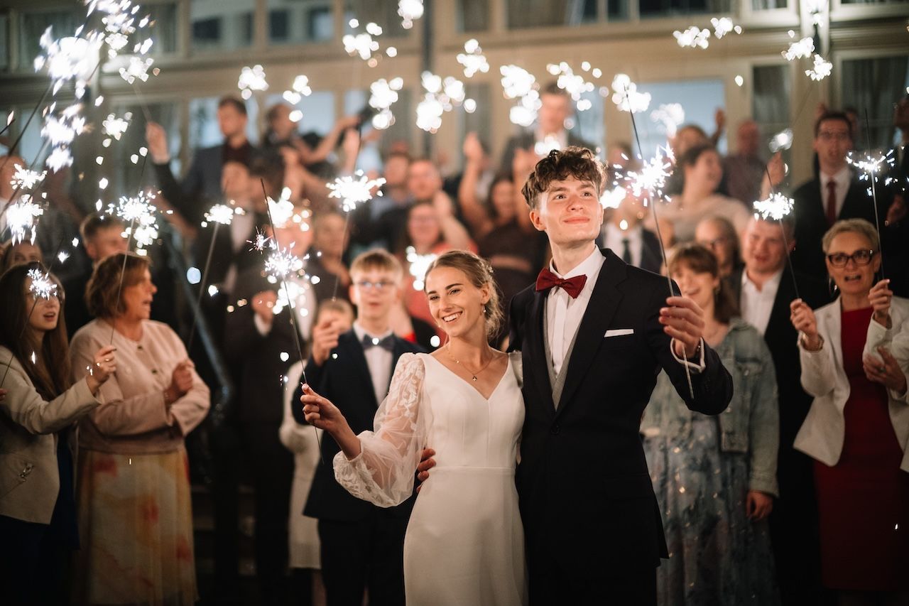 Bride and groom walk through sparkler tunnel surrounded by cheering wedding guests at night.