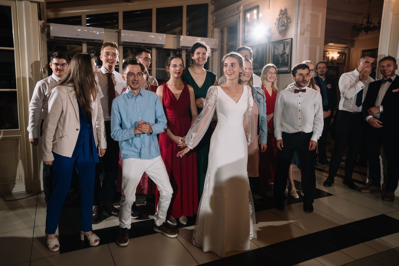 Bride and groom pose with wedding party guests on dance floor at reception.