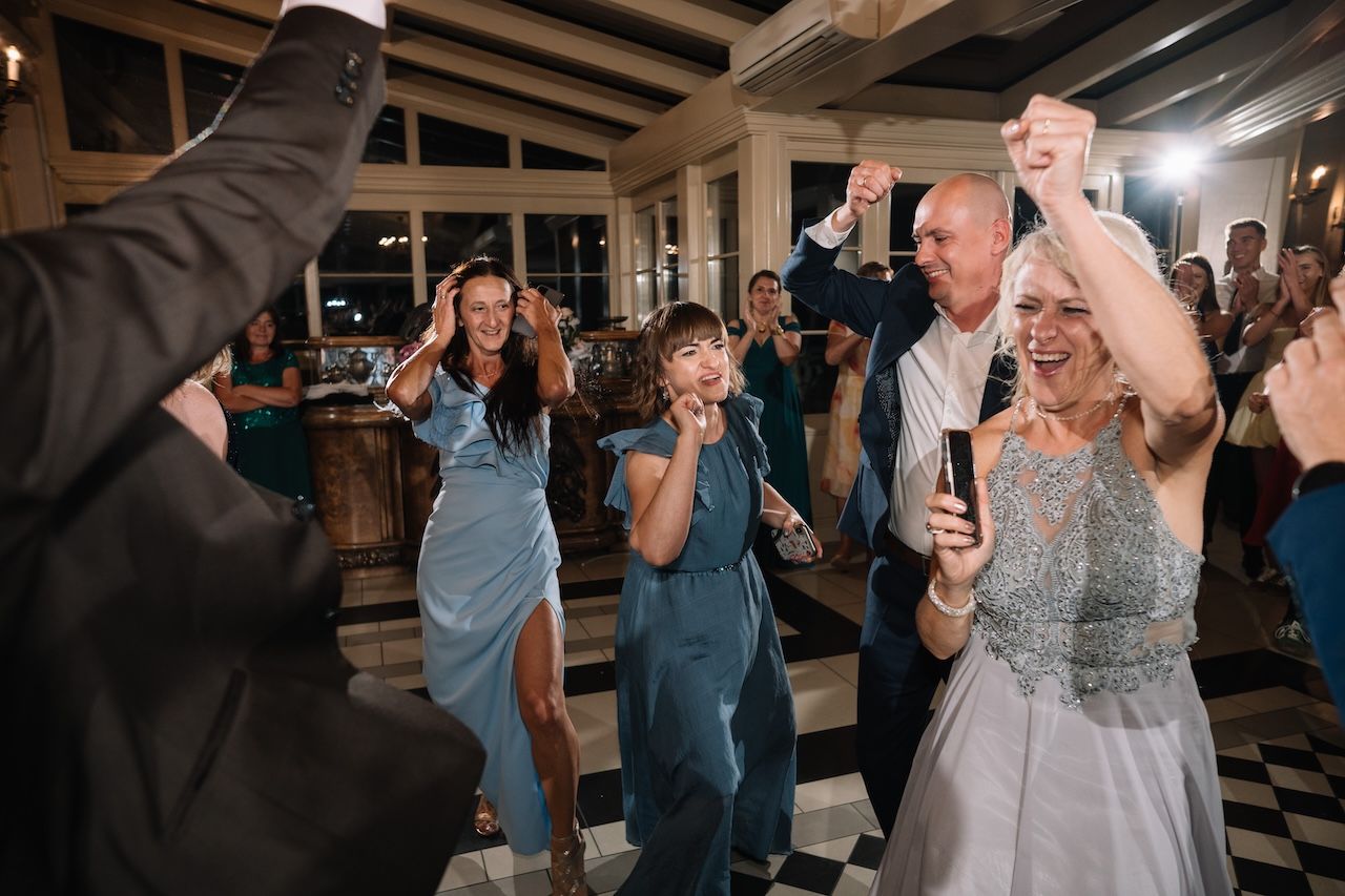 Joyful wedding guests dance and celebrate with raised arms at lively reception.