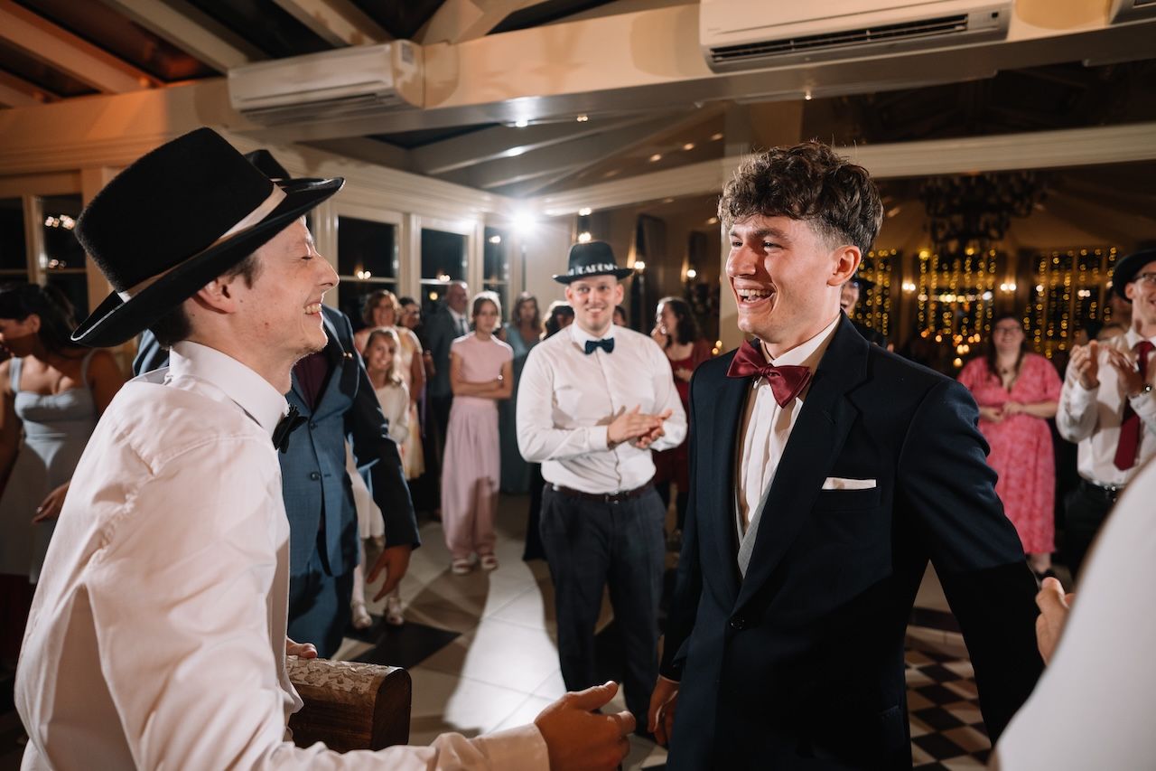 Two men laugh and shake hands on wedding reception dance floor.