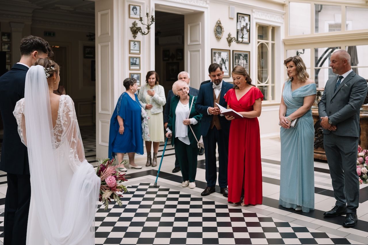 Wedding ceremony on black and white checkered floor with officiant reading vows to couple.