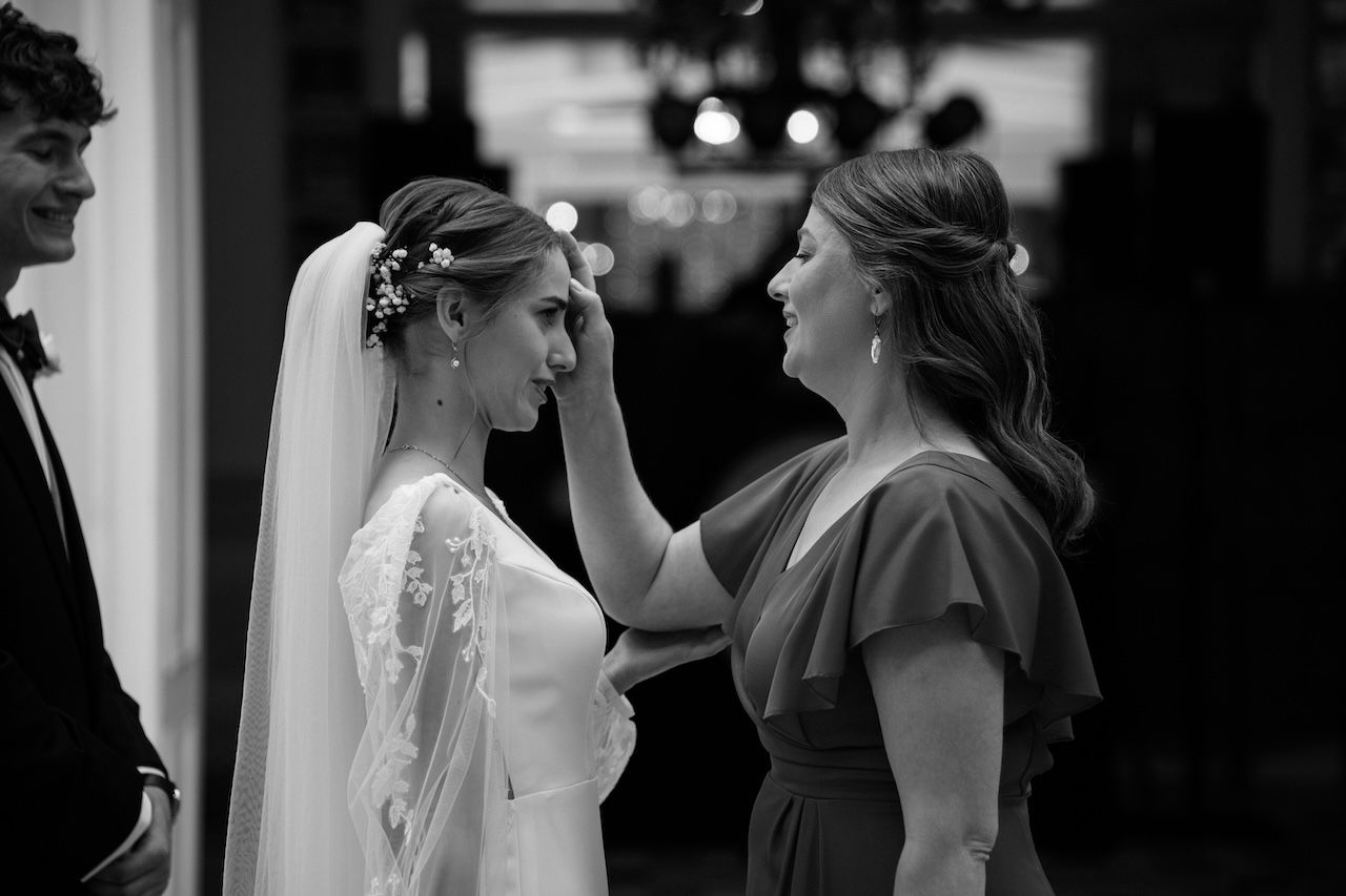 Black and white photo of bridesmaid tenderly adjusting bride's veil before wedding ceremony.
