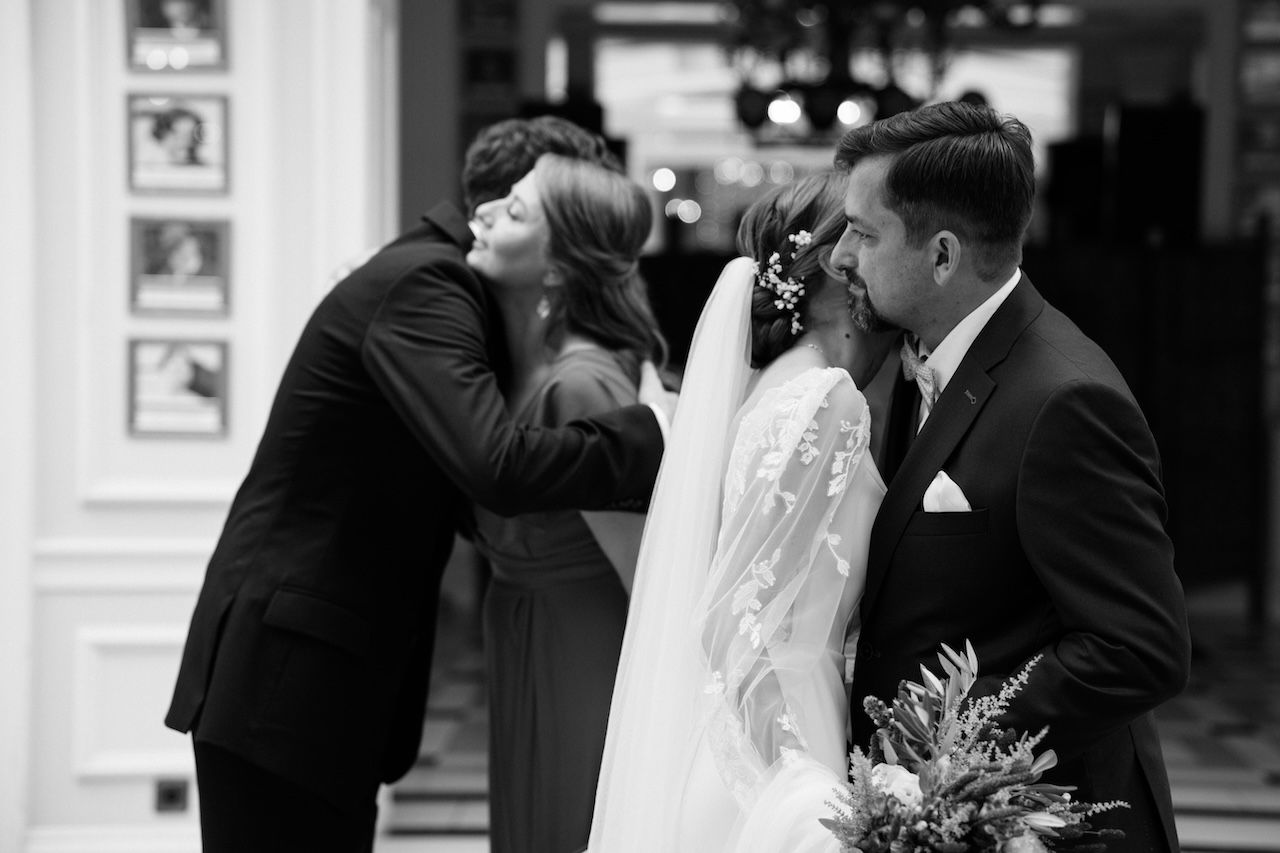 Black and white photo of wedding guests embracing bride and groom with bouquet after ceremony.