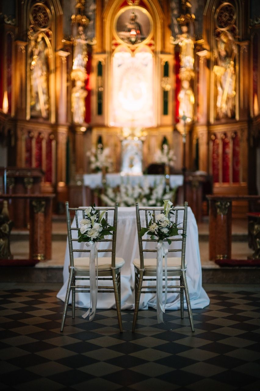 Elegant church wedding altar setup with two white chairs adorned with floral bouquets on a black and white checkered floor.