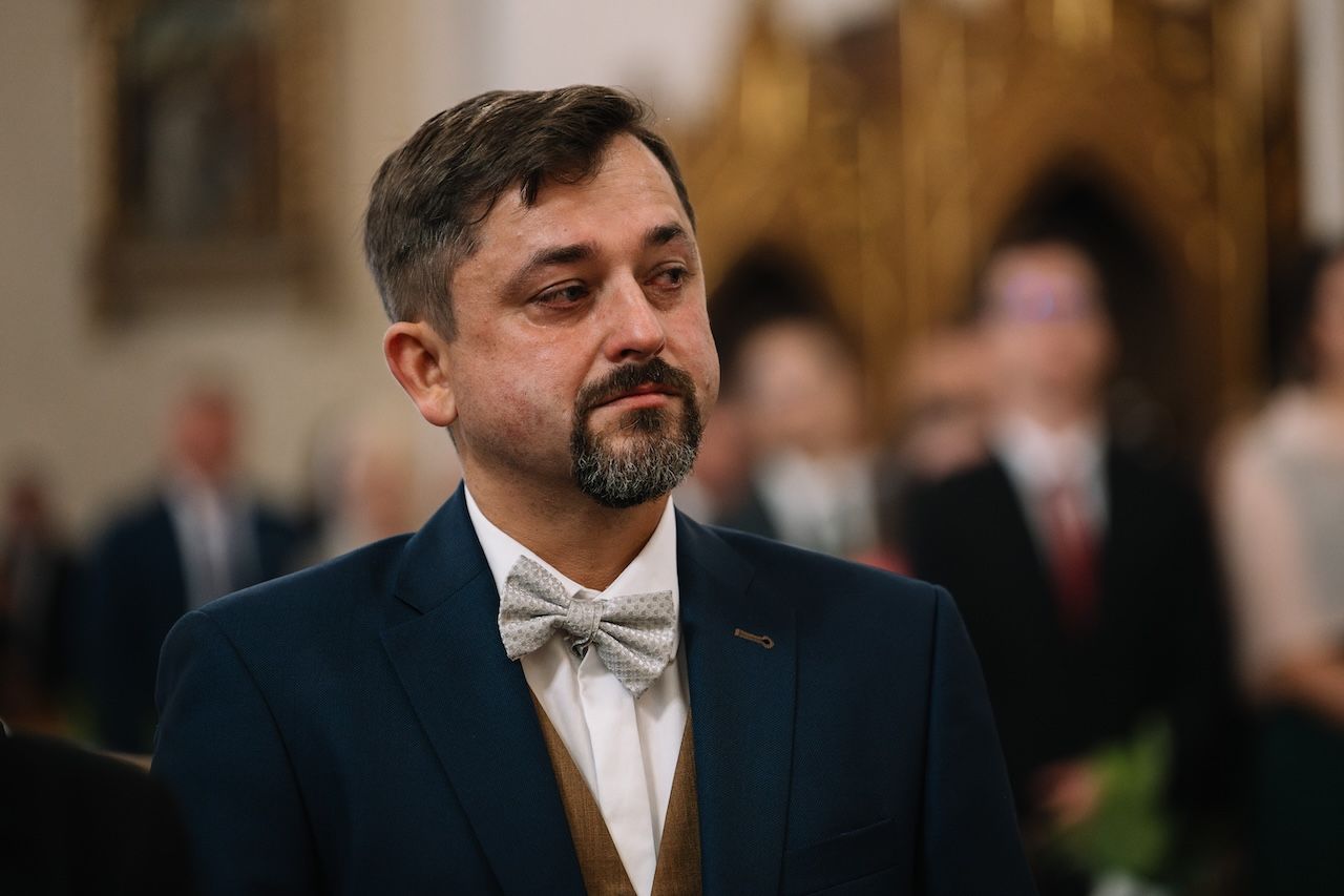 Emotional middle-aged man in navy suit with bow tie standing in a church during a wedding ceremony.