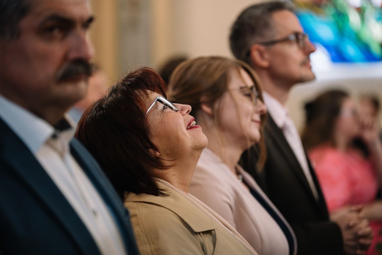 Emotional wedding guests laugh and smile while watching ceremony in ornate church.