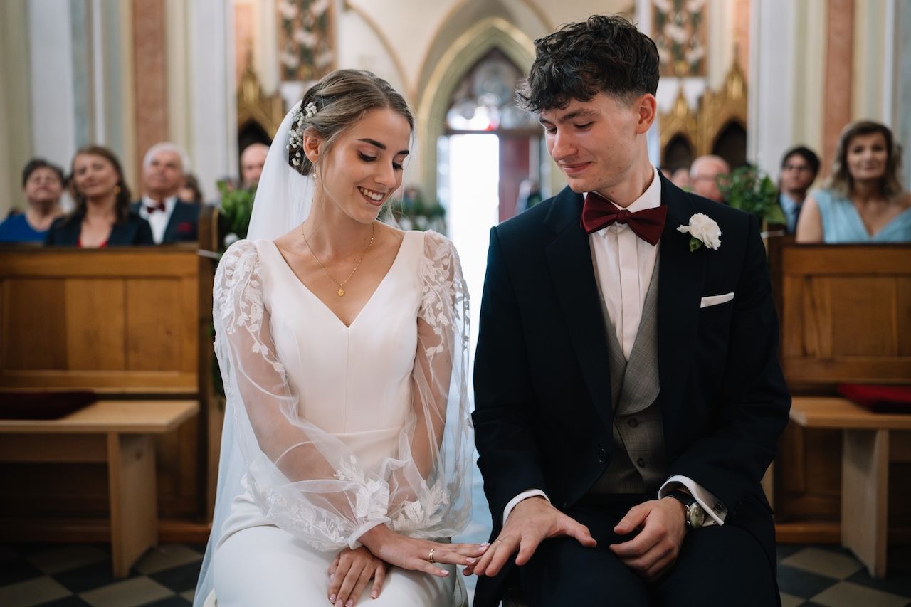 Bride and groom sitting together at church altar during wedding ceremony, smiling joyfully.