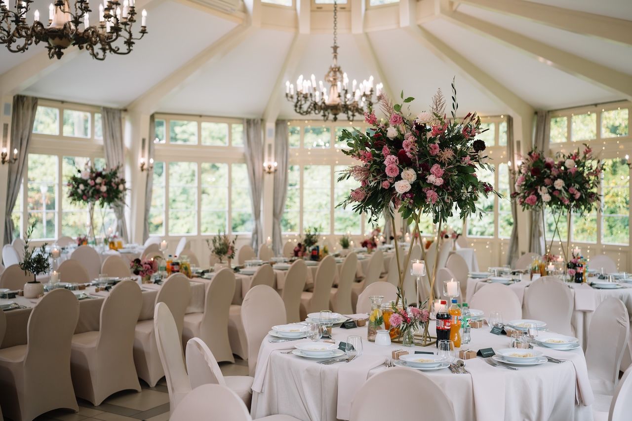 Elegant wedding reception hall with tall floral centerpieces, white tablecloths, and chandeliers.
