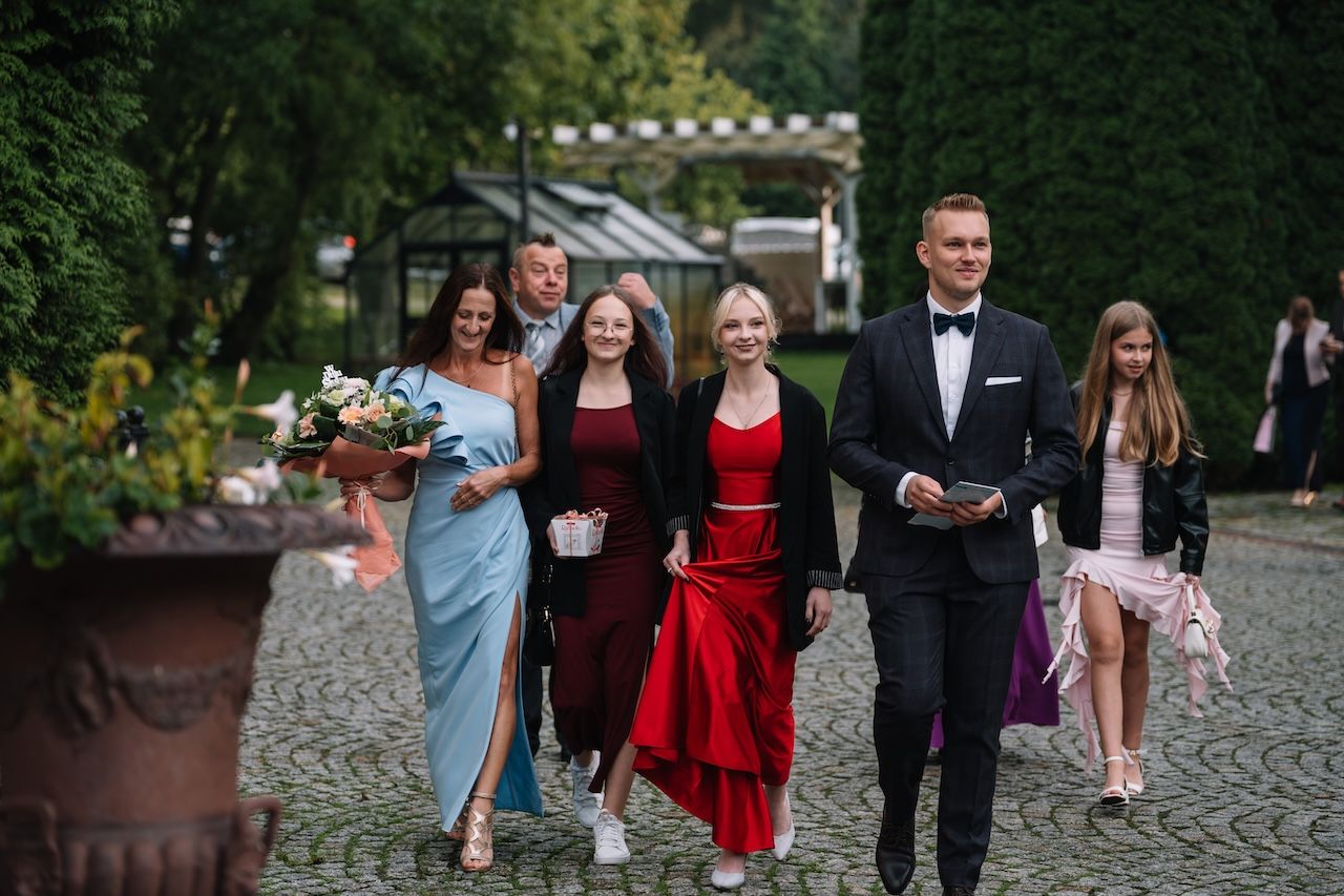 Wedding guests in formal attire walking along cobblestone path through lush garden venue.