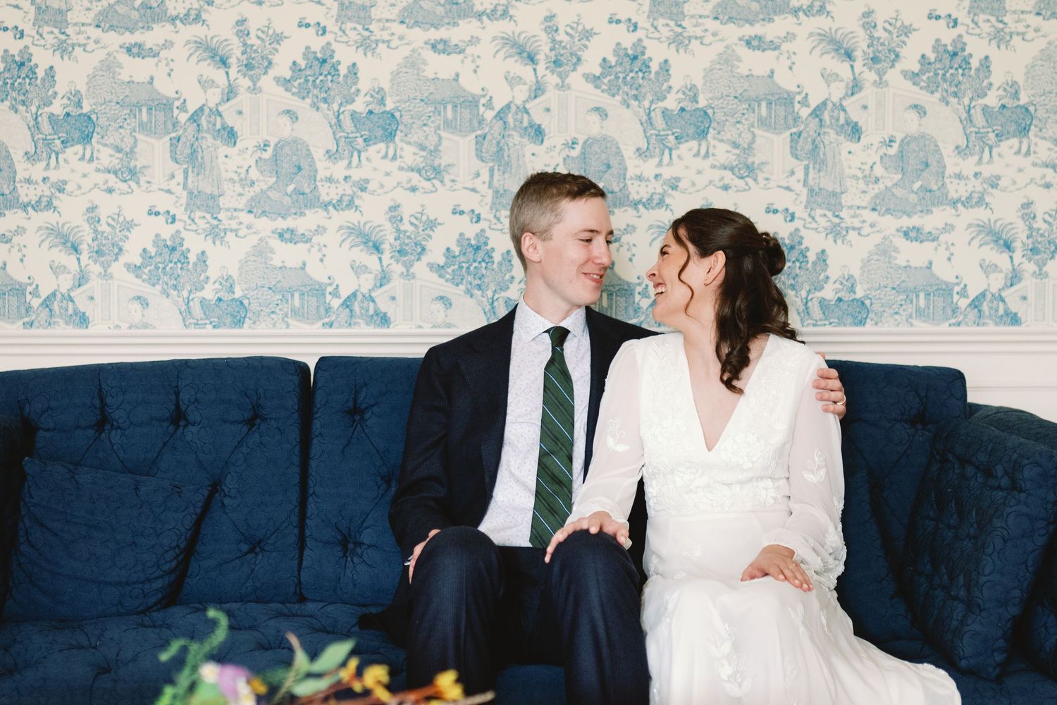 A couple sits close together on a navy blue sofa against floral wallpaper.