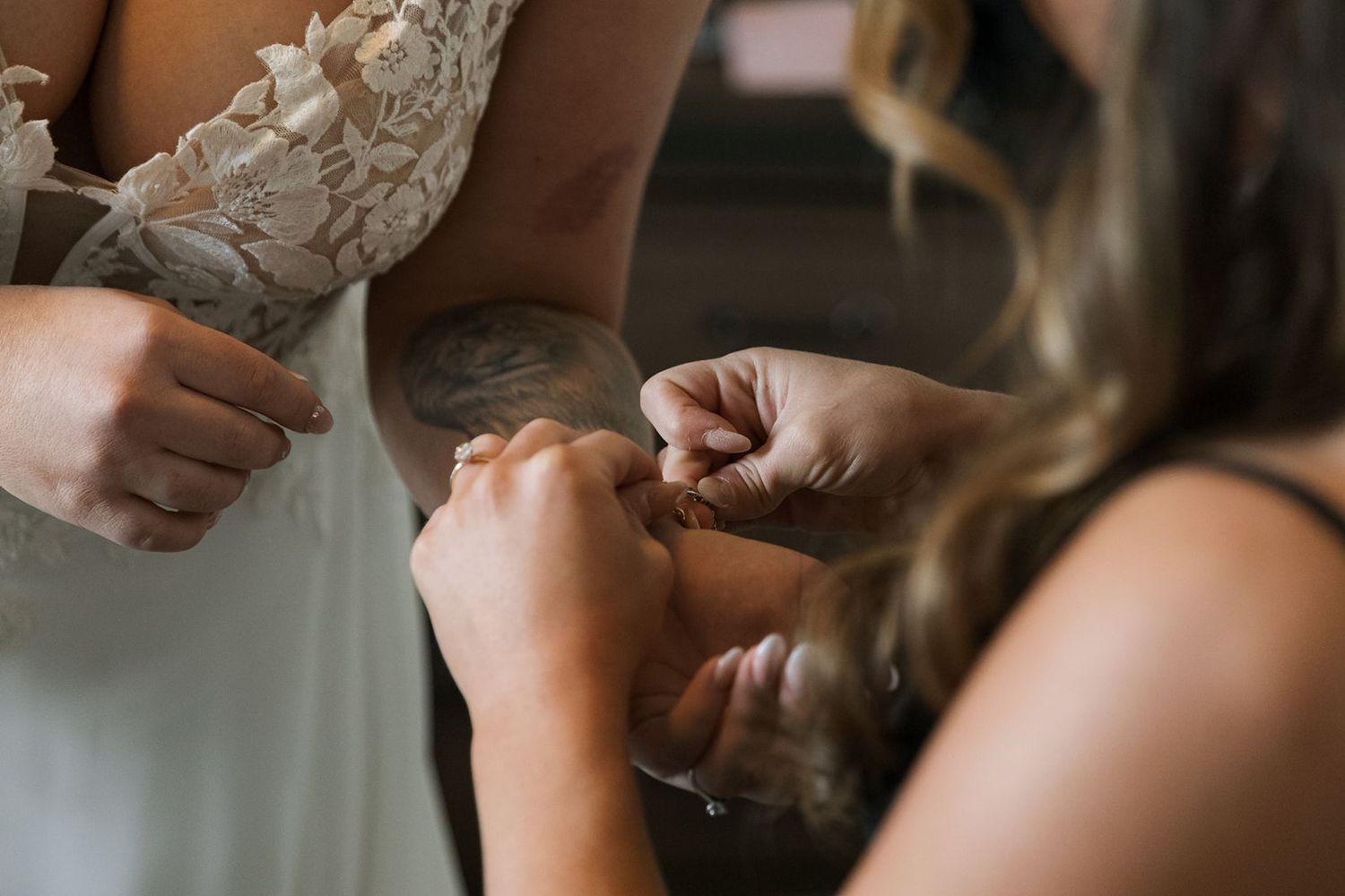 Bridesmaid helping bride with lace wedding dress buttons during bridal preparation.