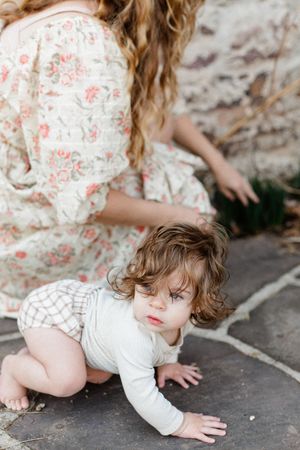A child in a floral dress crawls on a stone patio outdoors.