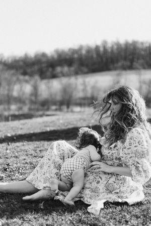 A black and white photograph of someone reclining on the ground in a floral dress against a natural outdoor backdrop.