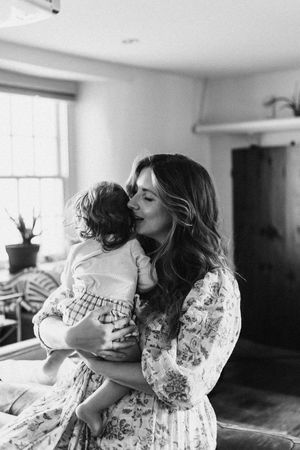 Tender moment between parent and child in a sunlit room with floral dress and natural decor.