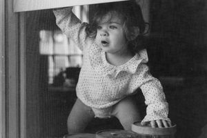 A black and white vintage photograph shows children gathered at a window looking outward with curiosity.