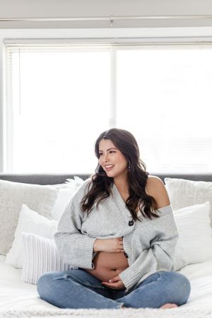Woman relaxing on white bedding in casual attire during an indoor photoshoot.