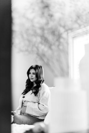 Black and white portrait of person in white sweater sitting by window with soft natural lighting.