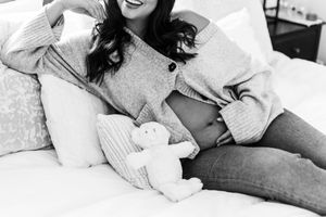 Black and white photo of person in gray sweater relaxing on bed with stuffed animal.