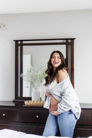 Woman in casual outfit laughing joyfully in bedroom with dark wood furniture.