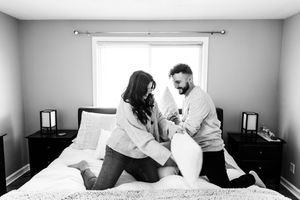 Couple in light colored clothing playing together on bed near window.