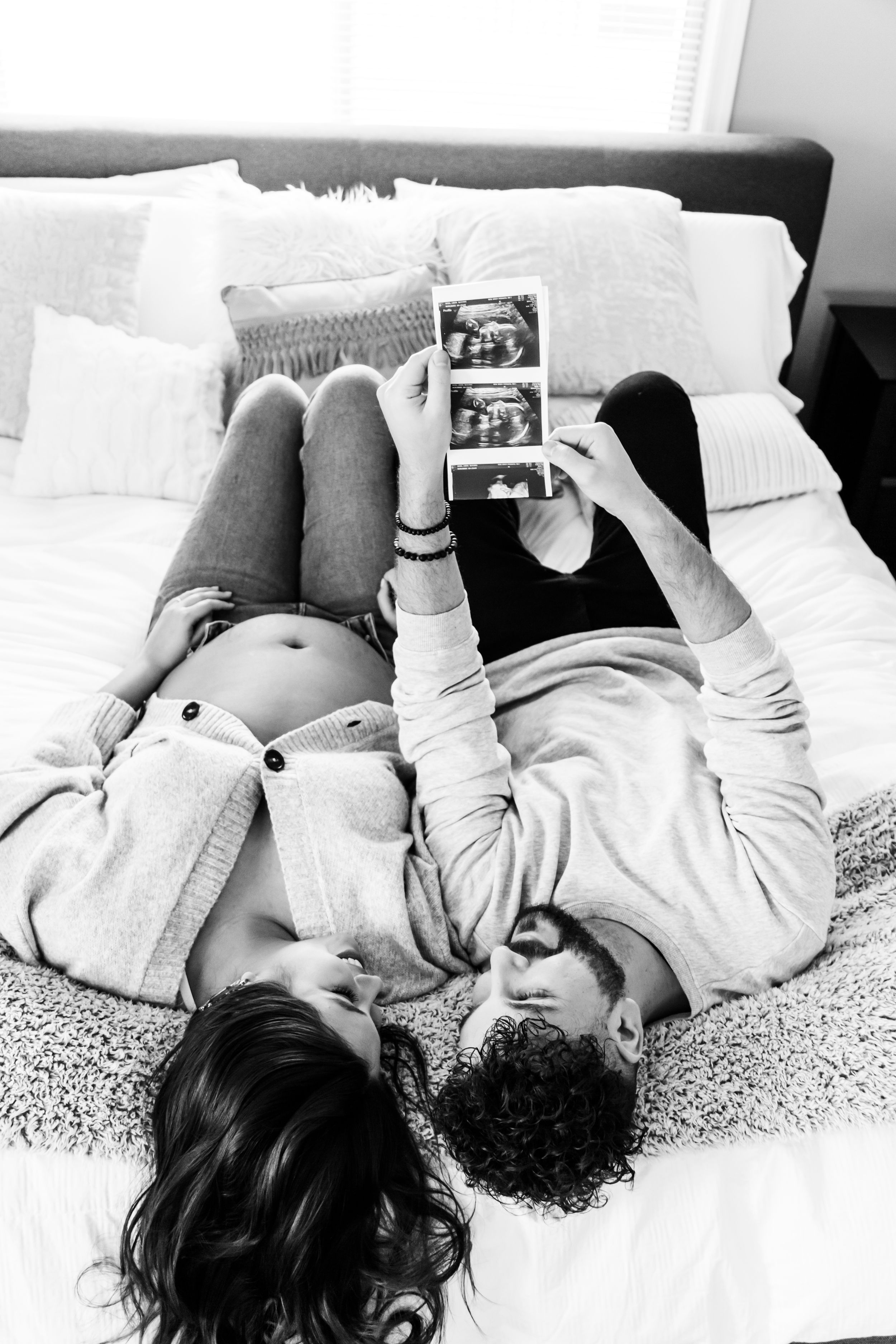 Black and white photo of a couple lying down and reading together on a bed.