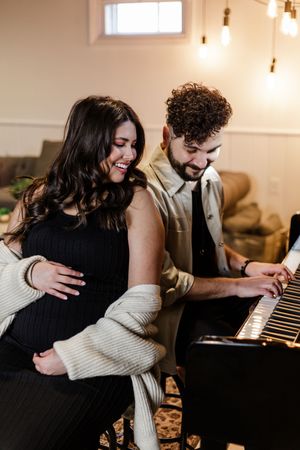 Couple sharing intimate moment while sitting at piano in dimly lit room.