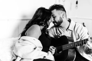 Couple sharing intimate moments while one plays acoustic guitar in black and white.