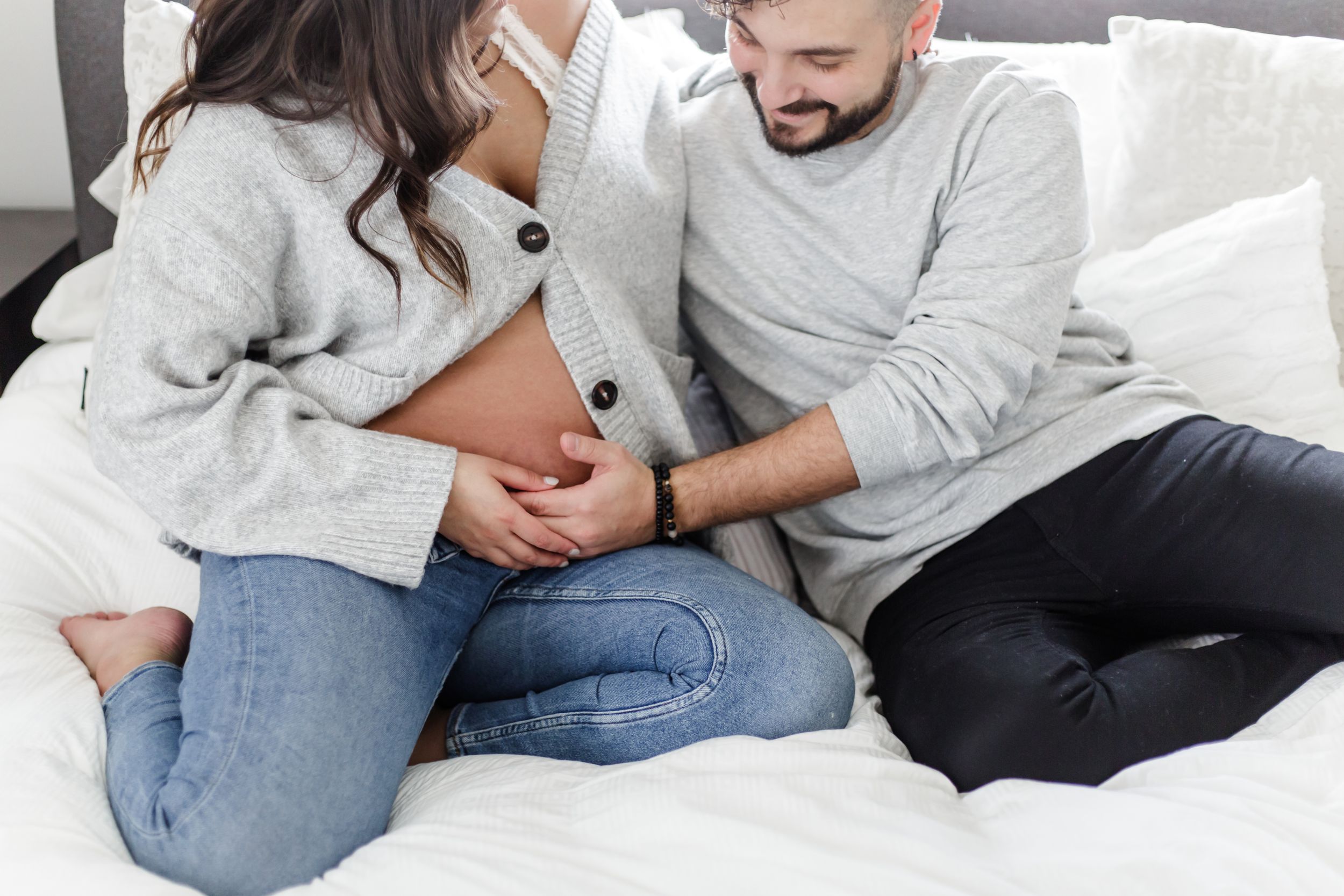 Couple in casual wear relaxing together on a cozy bed with white bedding and pillows.