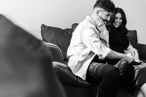 Playful couple having a pillow fight while lounging on a white couch in black and white photography.