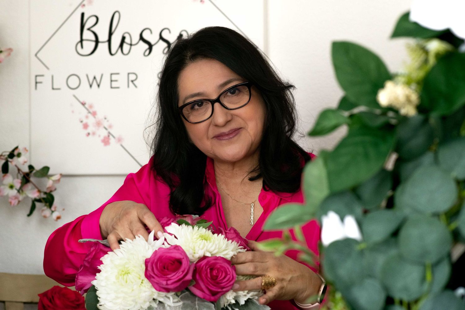Person working with pink roses and white flowers at Bloss Flower shop.