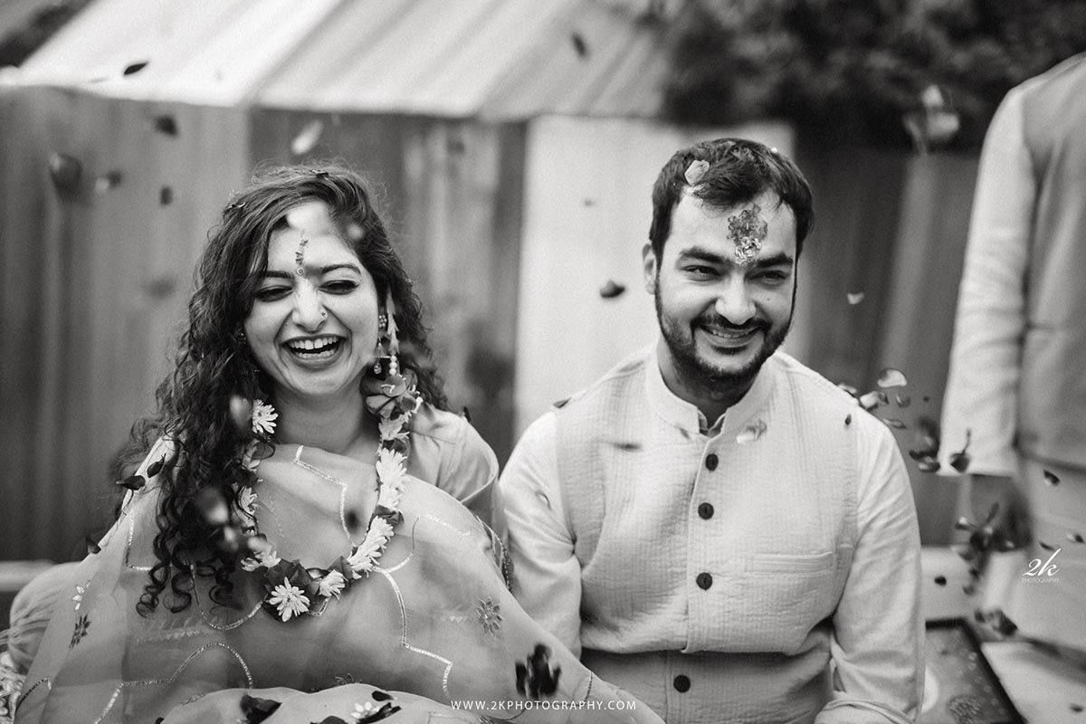 Black and white photo of a joyful moment at an outdoor celebration with traditional floral garlands and white attire.