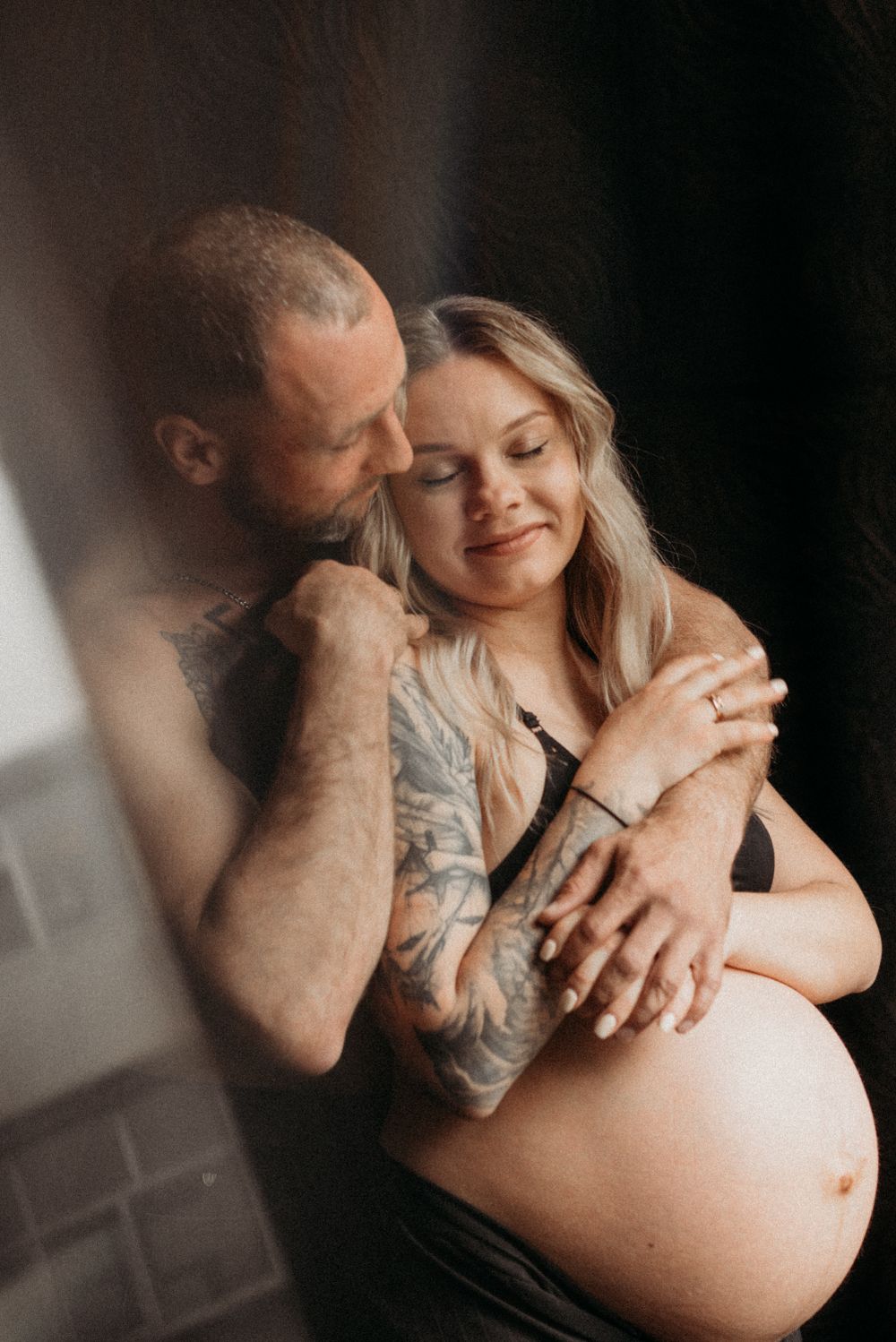 An intimate maternity photo showing a couple embracing in dramatic lighting.