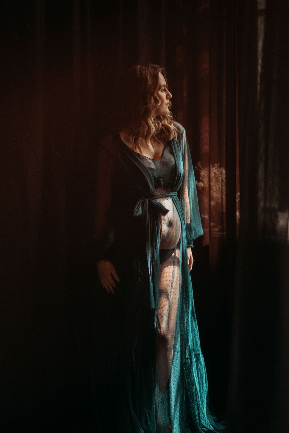 Artistic maternity portrait featuring a teal shawl against a dark background creating dramatic lighting effects.