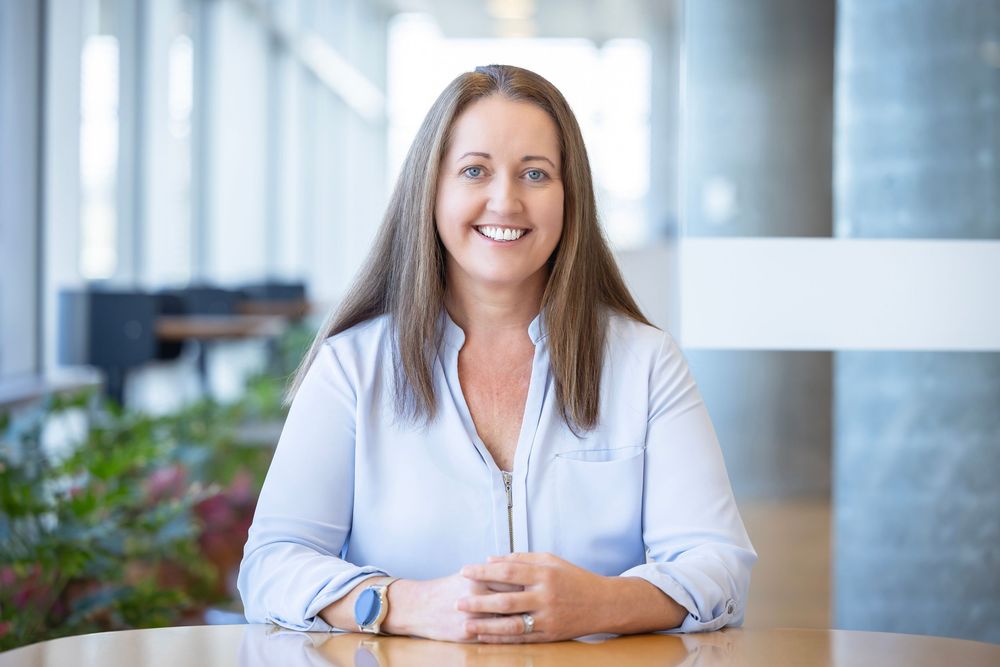 Portrait of a lady sitting at a table wearing a blue shirt with concrete columns in the background