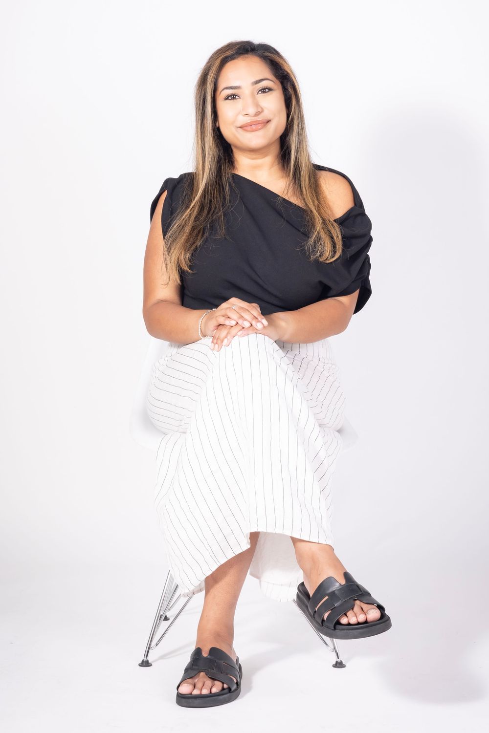 Tanya
Six Black Pens
Woman sitting on a chair in a black top and white pants on a white background looking at the camera