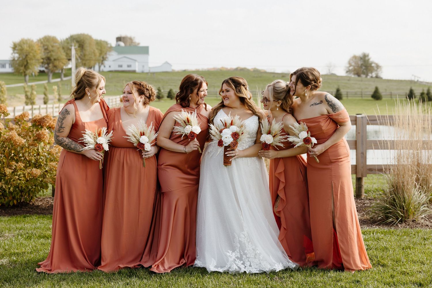 Wedding party in burnt orange bridesmaid dresses pose together outdoors during autumn celebration.