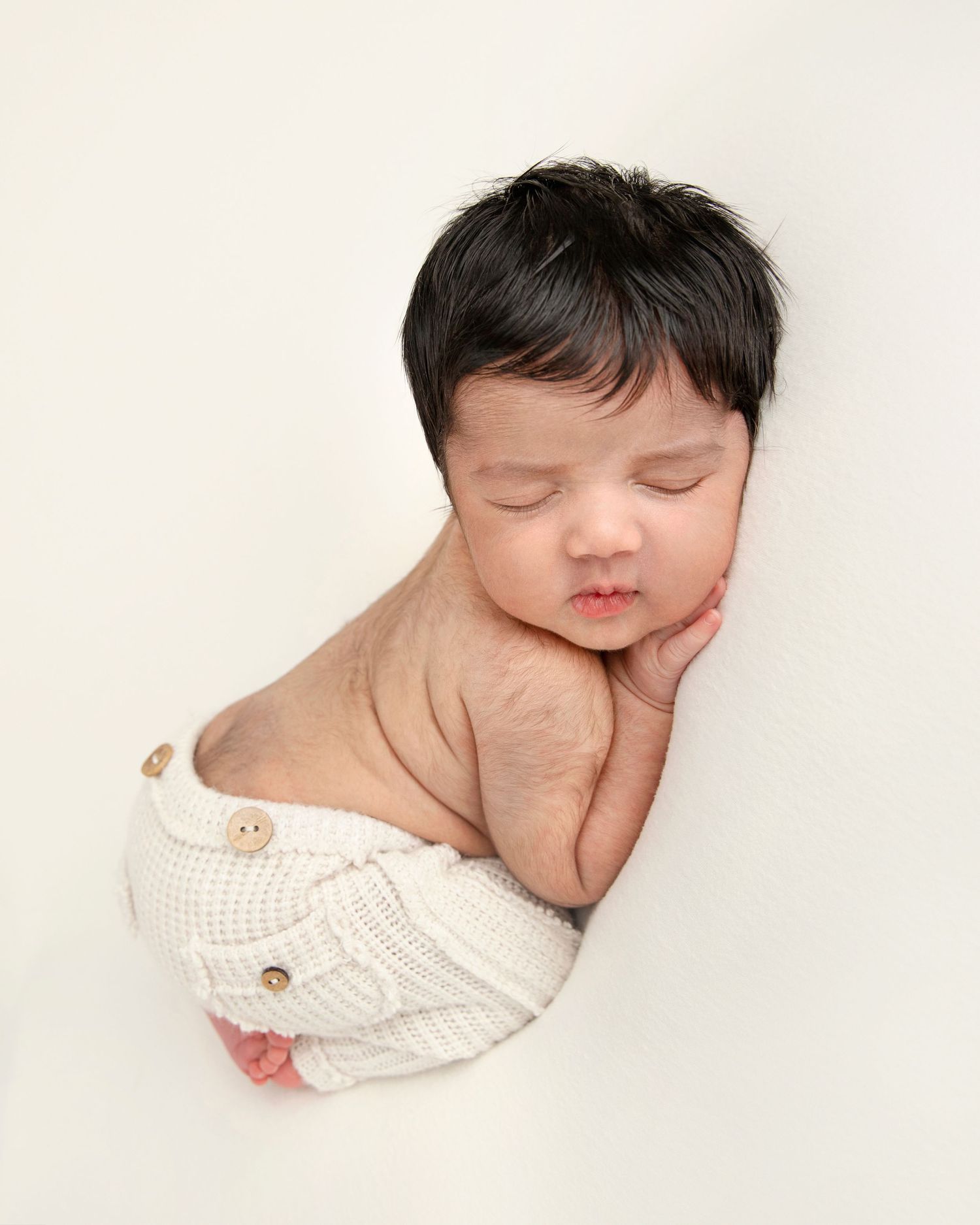 Sleeping baby in white knit diaper cover posed on cream background.