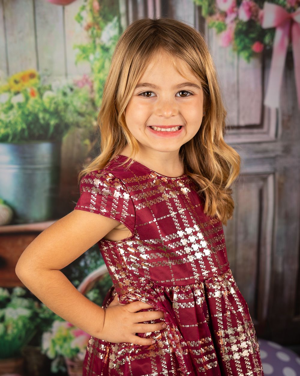 Child modeling burgundy plaid dress against floral garden backdrop with joyful expressions.