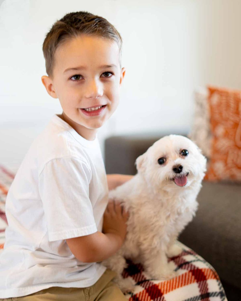 A smiling child sits on a couch with a small white fluffy dog.